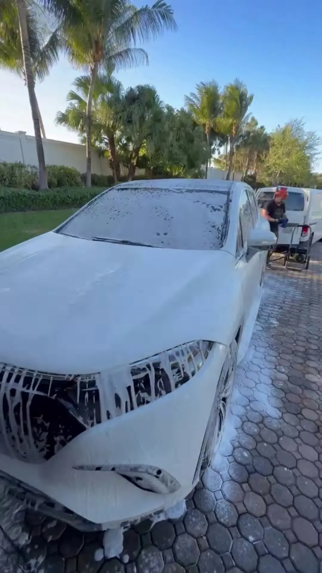 White Mercedes EQ SUV covered in foam during a hand wash, palm trees behind
